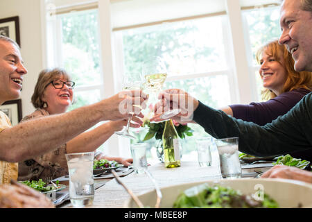 Senior couples toasting a home dinner party with glasses of white wine. Stock Photo