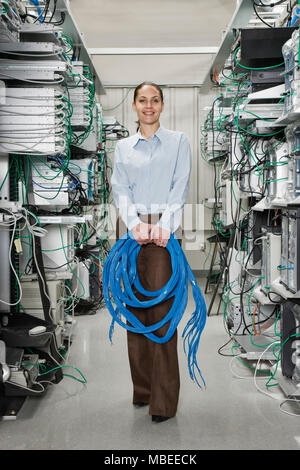 Female computer technician holding CAT 5 cables and standing in the aisle of a computer server farm. Stock Photo
