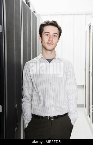 A male computer technician standing in an aisle of racks of servers in a computer server farm Stock Photo