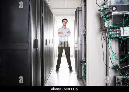 A male computer technician standing in an aisle of racks of servers in a computer server farm Stock Photo
