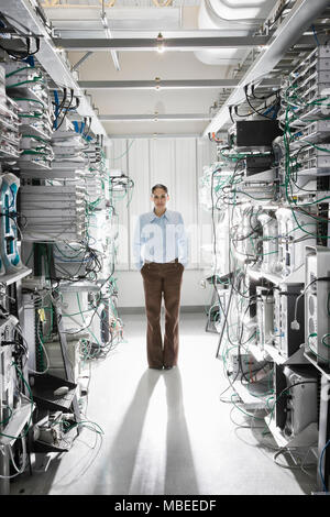 Caucasian woman technician working in the aisle of a computer server farm. Stock Photo