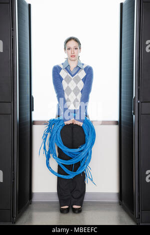 Female computer technician holding CAT 5 cables and standing in the aisle of a computer server farm. Stock Photo