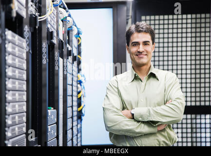 A male computer technician standing in an aisle of racks of servers in a computer server farm Stock Photo