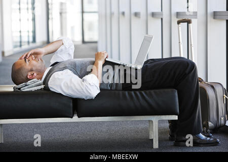 Exhausted businessman taking a short break laying on a bench in an office lobby. Stock Photo