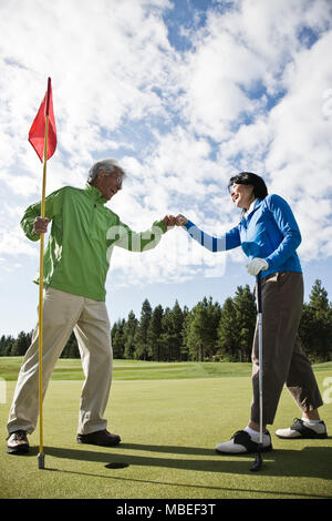 A senior couple doing a fist bump after making putt on a green. Stock Photo