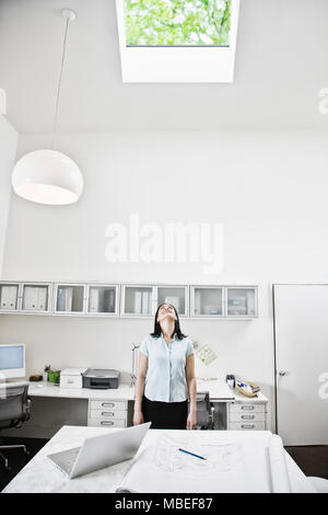 HIspanic woman looking up at a skylight in an architect's office. Stock Photo