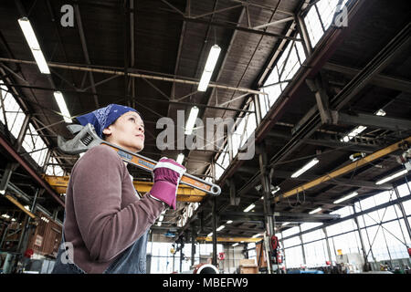 Black woman factory worker holding a large wrench in a sheet metal factory. Stock Photo