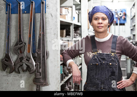 Black woman factory worker wearing coveralls in a large sheet metal factory. Stock Photo