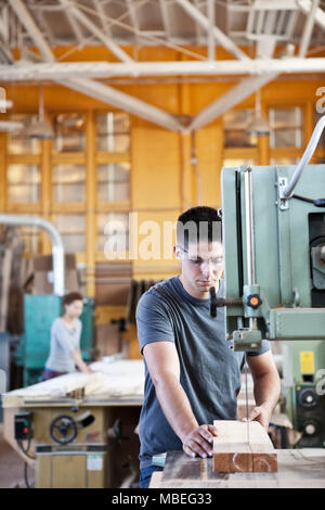 Caucasian man curring wood using a band saw in a woodworking factory. Stock Photo