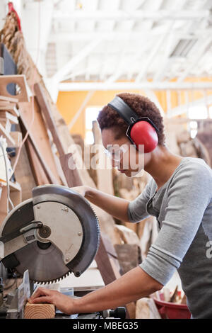 Black woman factory worker using a radial saw to cut wood in a woodworking factory. Stock Photo