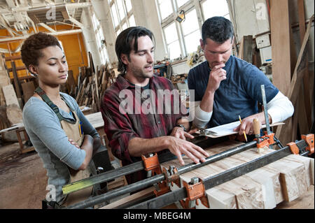 Team of multi-racial workers discussing an issue related to glueing a part together in a woodworking factory. Stock Photo