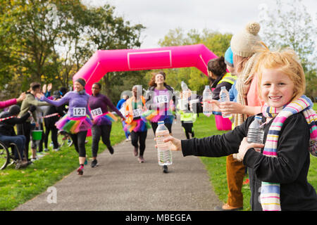 Portrait smiling girl spectator with water for runners at charity run in park Stock Photo