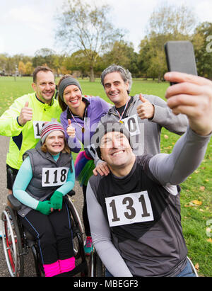Man in wheelchair taking selfie with friends at charity race in park Stock Photo