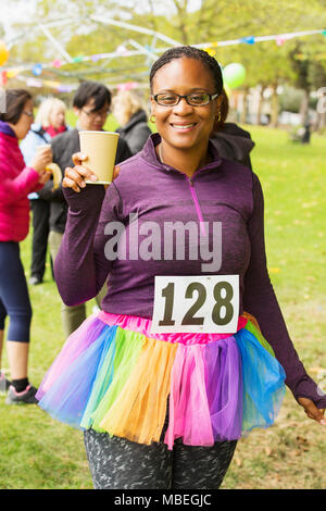 Portrait smiling female runner in tutu drinking water at charity run in park Stock Photo