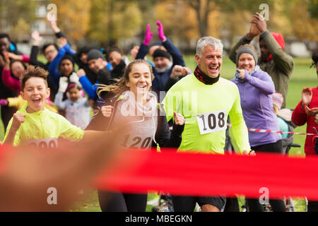 Enthusiastic family running, nearing finish line at charity run in park Stock Photo