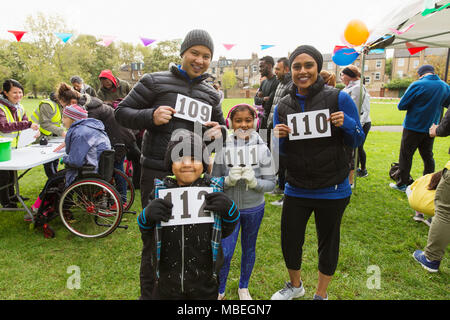 Portrait confident family runners showing marathon bibs at charity run in park Stock Photo