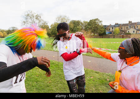 Playful runners celebrating, throwing holi powder at charity run in park Stock Photo