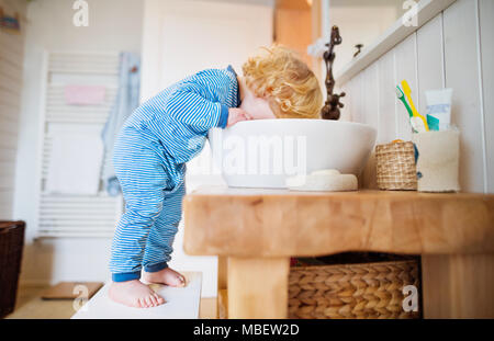 Cute toddler in the bathroom. Little boy putting a head in a sink. Domestic accident. Dangerous situation. Stock Photo