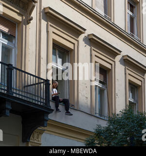 Man sitting on window ledge using a cell phone, Budapest, Hungary Stock Photo
