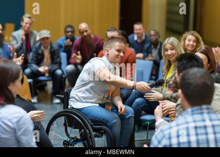 Female speaker in wheelchair giving microphone to audience Stock Photo