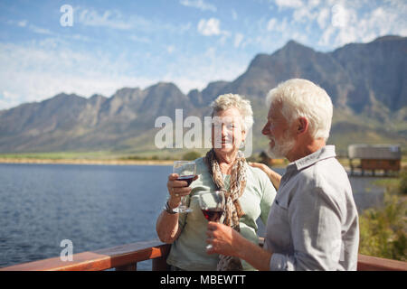 Smiling active senior couple drinking red wine on sunny summer lake balcony Stock Photo