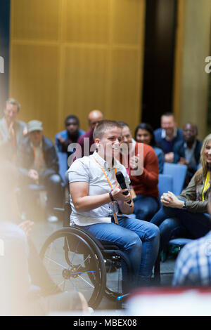 Smiling woman in wheelchair speaking with microphone in audience Stock Photo