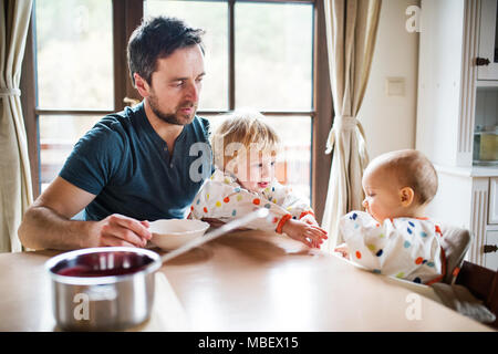 Father feeding two toddlers at home. Paternity leave.