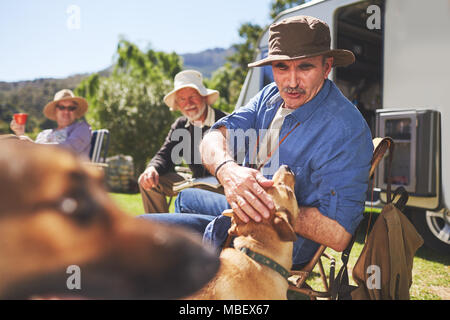Active senior man petting dog at sunny summer campsite Stock Photo