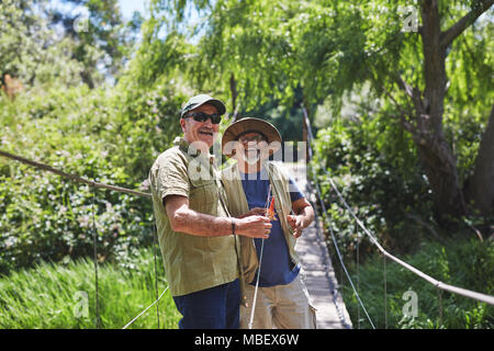 Portrait happy active senior men friends fishing on sunny summer footbridge Stock Photo