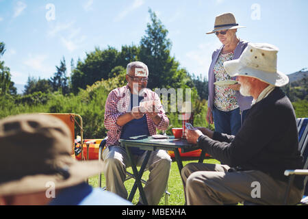 Playful active senior friends playing cards at sunny summer campsite Stock Photo