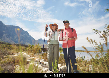 Active senior couple hiking with hiking poles at sunny summer lakeside Stock Photo