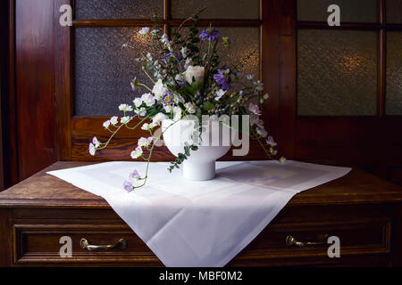 Elegant still-life from a bouquet of spring flowers in a white vase in an interior of noble wood Stock Photo