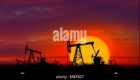 Oil pumps silhouettes working on clouds and sun in background. Pumpjack on oilfield on sunset. Concept of oil rig, global warming, environment polluti Stock Photo