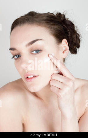 Woman applying face cream and looking towards the camera into a mirror Stock Photo