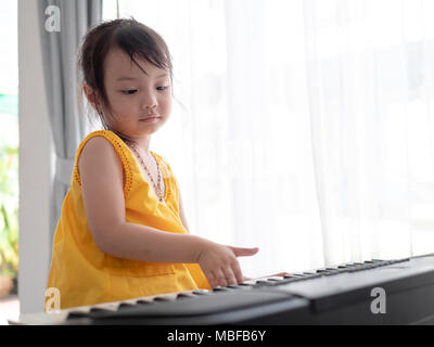 Asian girl playing keyboard piano near window at home. Stock Photo