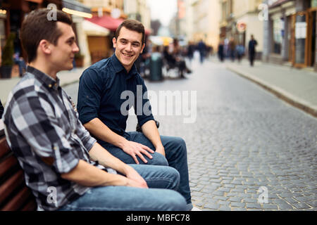 Two man sit on bench and talk on the street Stock Photo