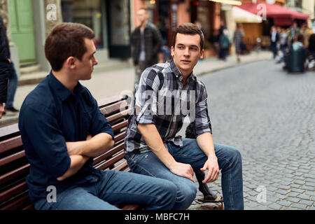 Two man sit on bench and talk on the street Stock Photo