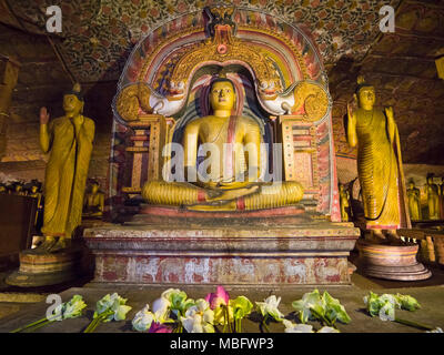 Horizontal view of flowers infront the seated Buddha at the Dambulla Cave Temple in Sri Lanka. Stock Photo