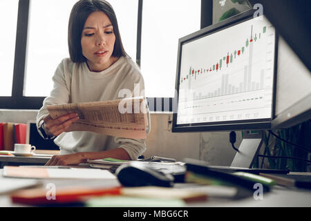 ?omparison of indicators of the currency market in the newspaper . Indoor, studio shot. Business people concept, work in office Stock Photo