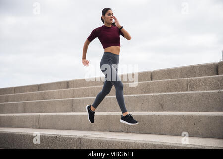 Pretty young brunette running on stairs wearing fitness clothing with her hair tied back Stock Photo