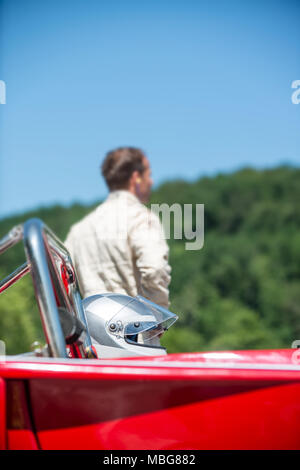 Unidentifiable man in race suit behind his race car and helmet, waiting for the start. Selective focus on the helmet in the foreground. Stock Photo