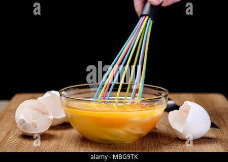 Mixing egg with a colorful whisk eggshells on wooden backround, close up Stock Photo