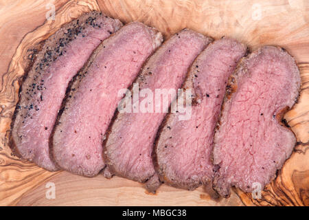 Grass fed juicy corn roast beef on olive wood cutting board isolated on white background Stock Photo