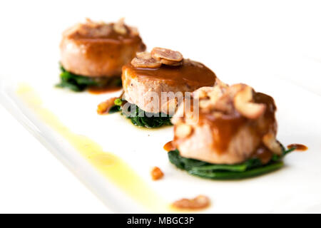 lateral shot of three veal fillet medallions with white wine sauce and boiled chestnuts on spinach leafs on white background Stock Photo