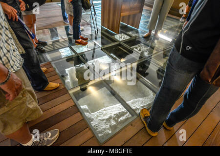 Tourists peer through the glass floor in the ancient catacombs of St Paul in the Mediterranean city of Rabat on the island of Malta. Stock Photo