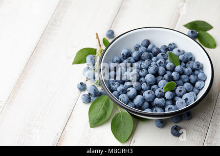 Fresh ripe blueberries with leaves in bowl on white wooden planks Stock Photo