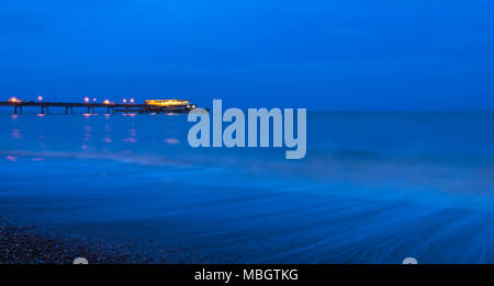 Waves crashing along Deal seafront at dusk with Deal Pier illuminated in the background. Stock Photo