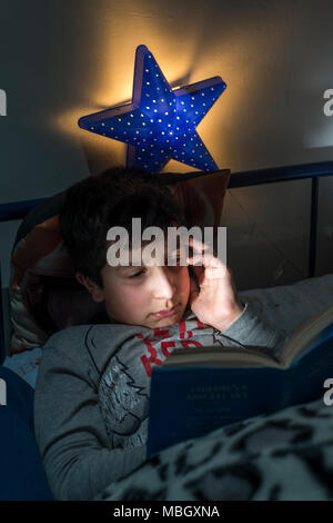 UK,Surrey, boy reads in bed late at night Stock Photo