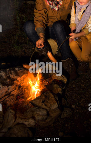 Into the wild. smiling healthy mother and daughter travellers near a bonfire grilling sausages Stock Photo