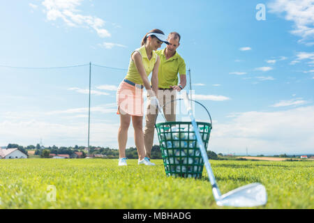 Cheerful young woman learning the correct grip and move for using the golf club Stock Photo